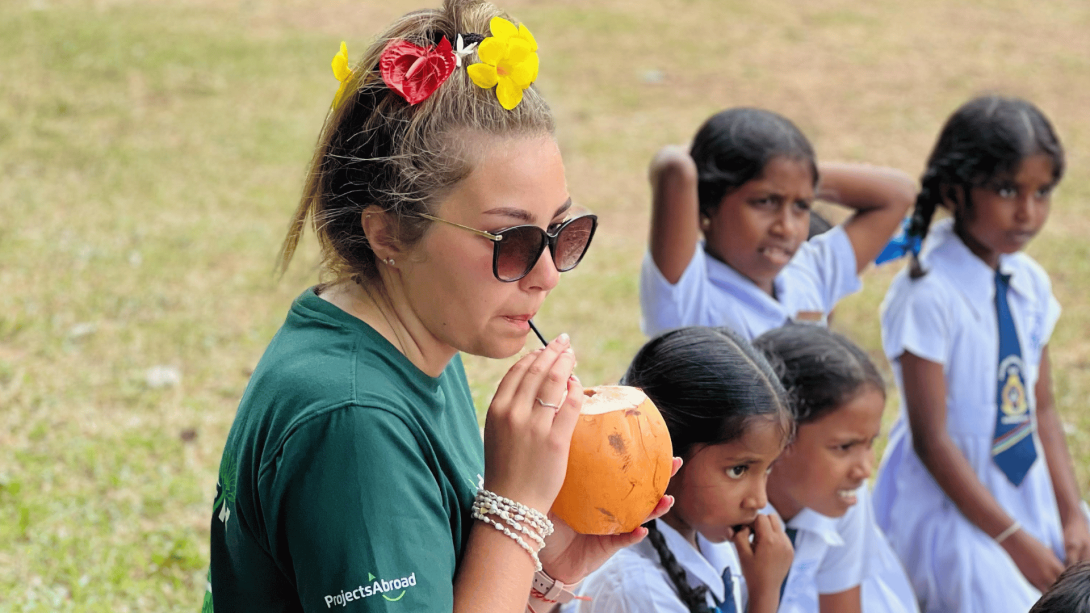 Participant in Sri Lanka tries coconut water alongside local children